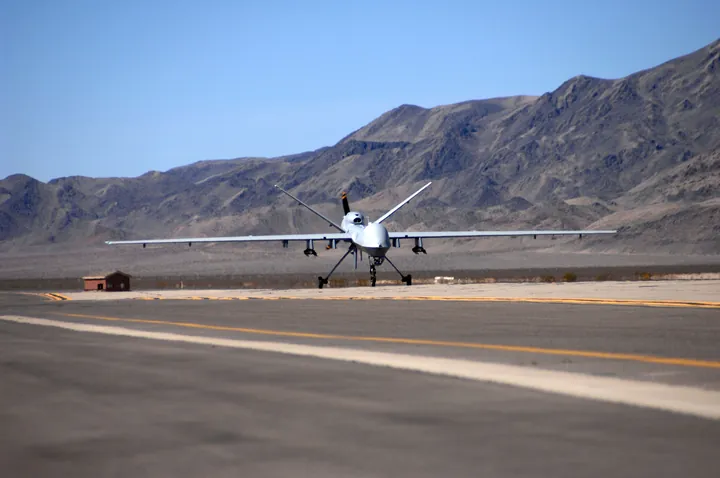 An MQ-9 Reaper drone on the runway at Creech Air Force Base, with bare desert mountains behind